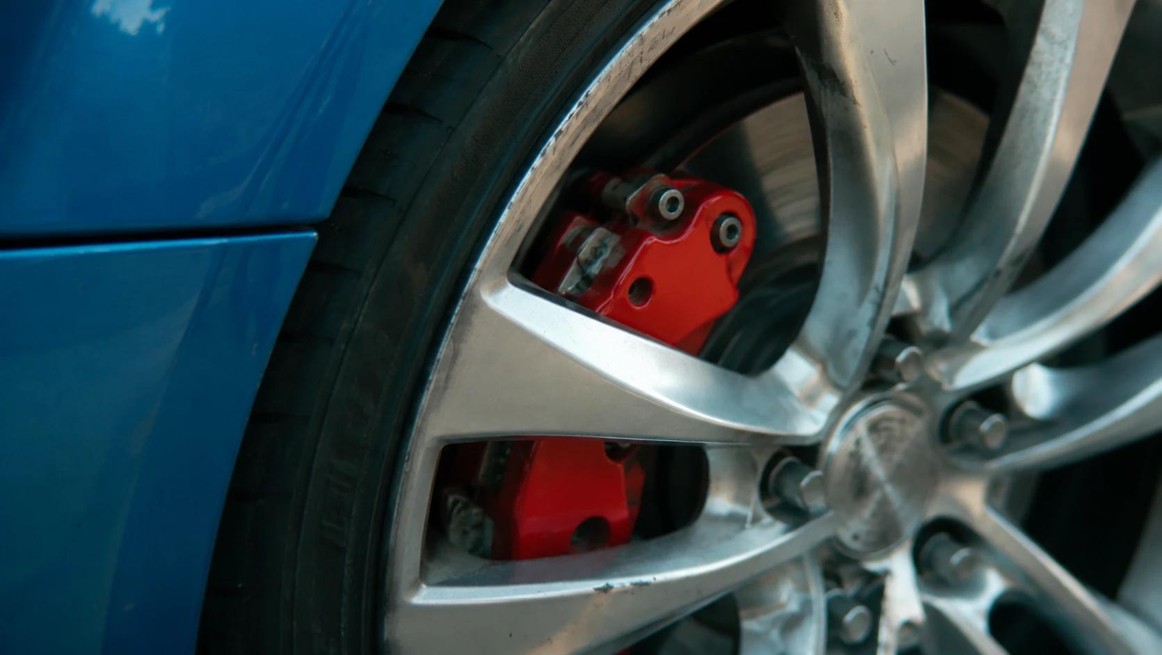Primer plano de una llanta de aleación con caliper de freno rojo y disco en un auto azul
